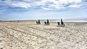 Una playa con filas de sillas y sombrillas vacías, un cielo despejado y el océano al fondo.