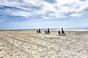 Une plage bordée de rangées de chaises longues et de parasols vides, un ciel dégagé et l’océan en toile de fond.