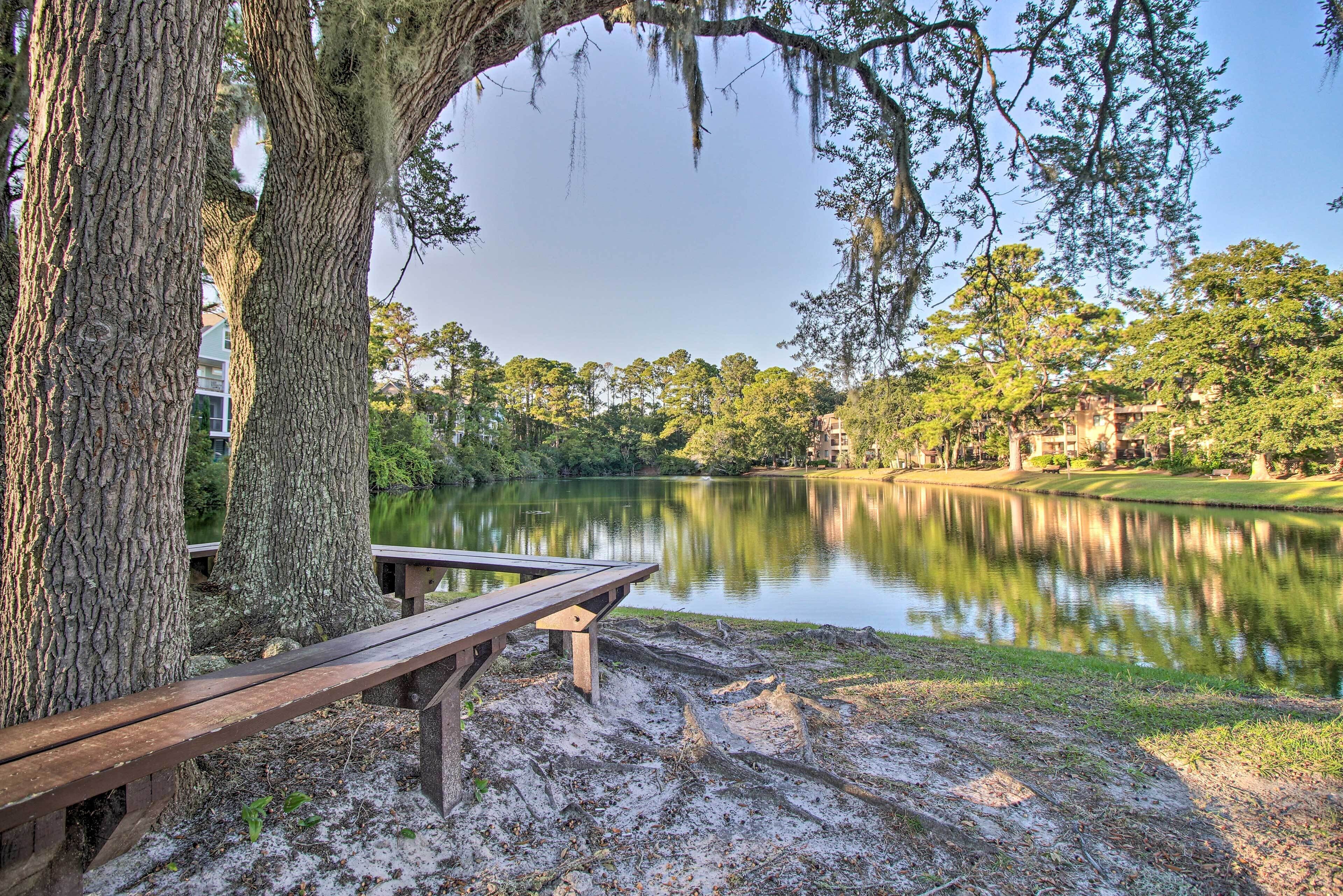 A wooden bench by a lake with trees and a building in the background.