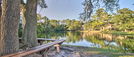 A wooden bench by a lake with trees and a building in the background.