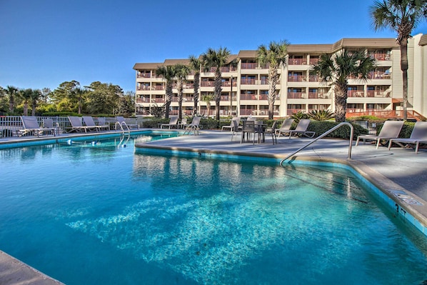 Piscina com espreguiçadeiras e um edifício de hotel em vários andares ao fundo.