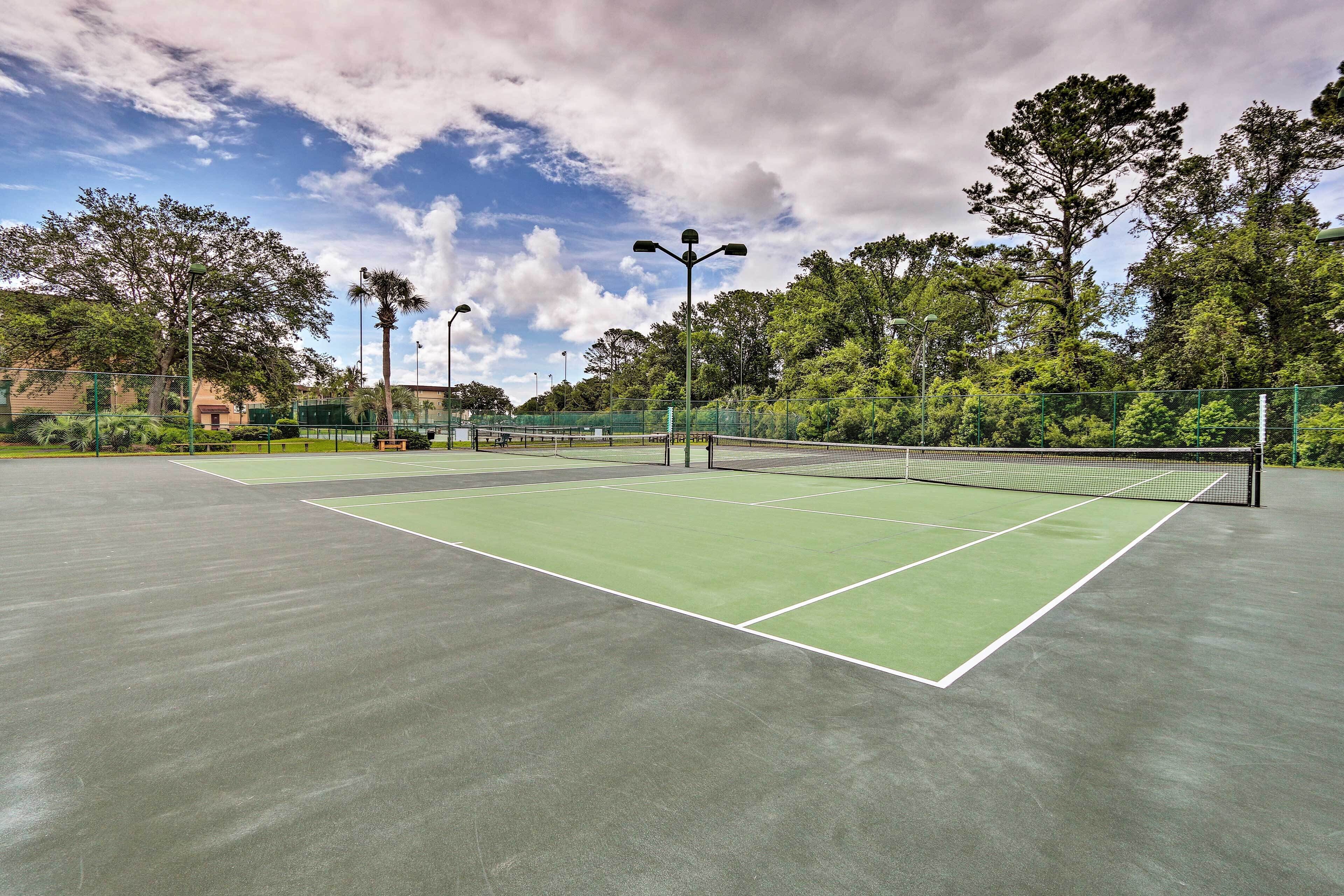Un court de tennis extérieur doté d’une surface verte, entouré d’arbres et d’une clôture.