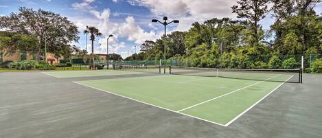 Un court de tennis extérieur doté d’une surface verte, entouré d’arbres et d’une clôture.