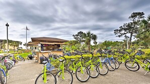 Una estación de alquiler de bicicletas con varias bicicletas, un pequeño quiosco y un área vallada con vegetación.