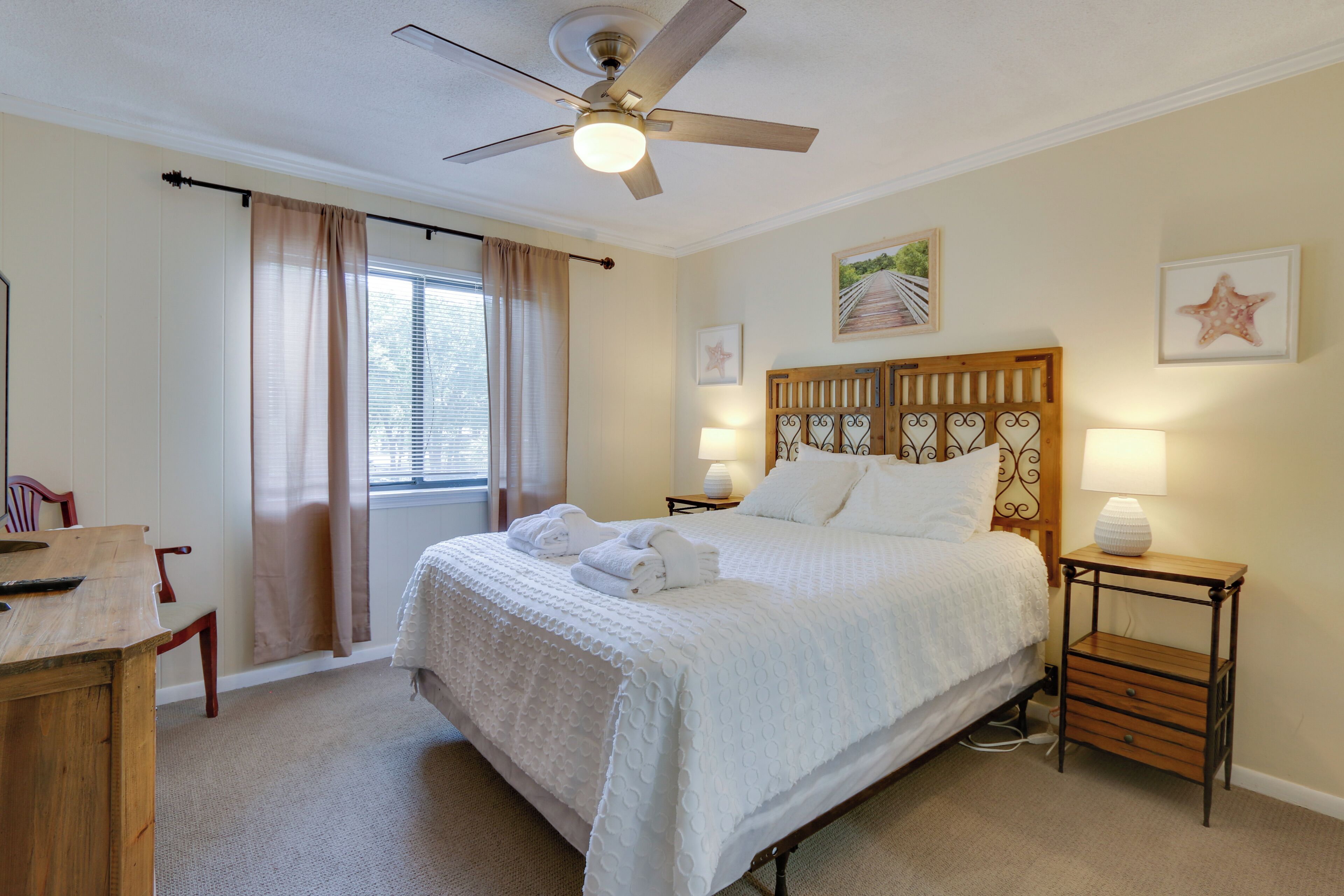 A bedroom with a bed, bedside tables, a ceiling fan, and a window with curtains.