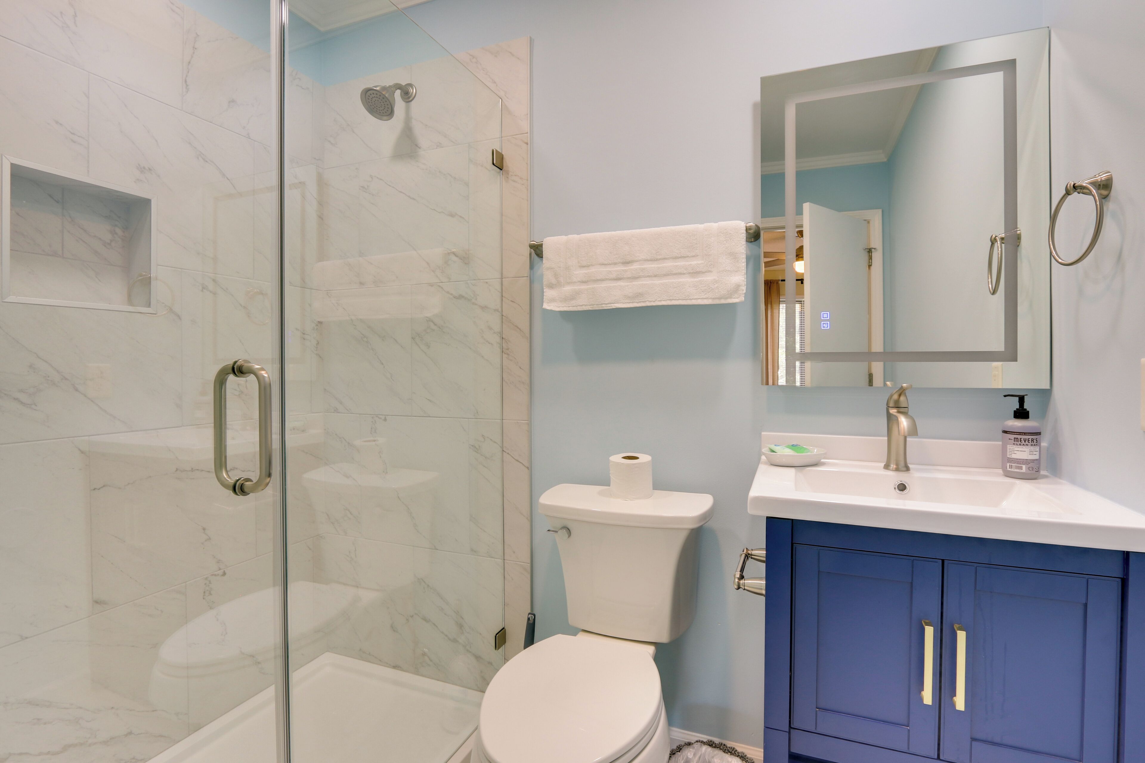 A bathroom with a glass-enclosed shower, a toilet, a sink with a mirror, and blue cabinets.