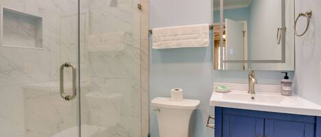 A bathroom with a glass-enclosed shower, a toilet, a sink with a mirror, and blue cabinets.