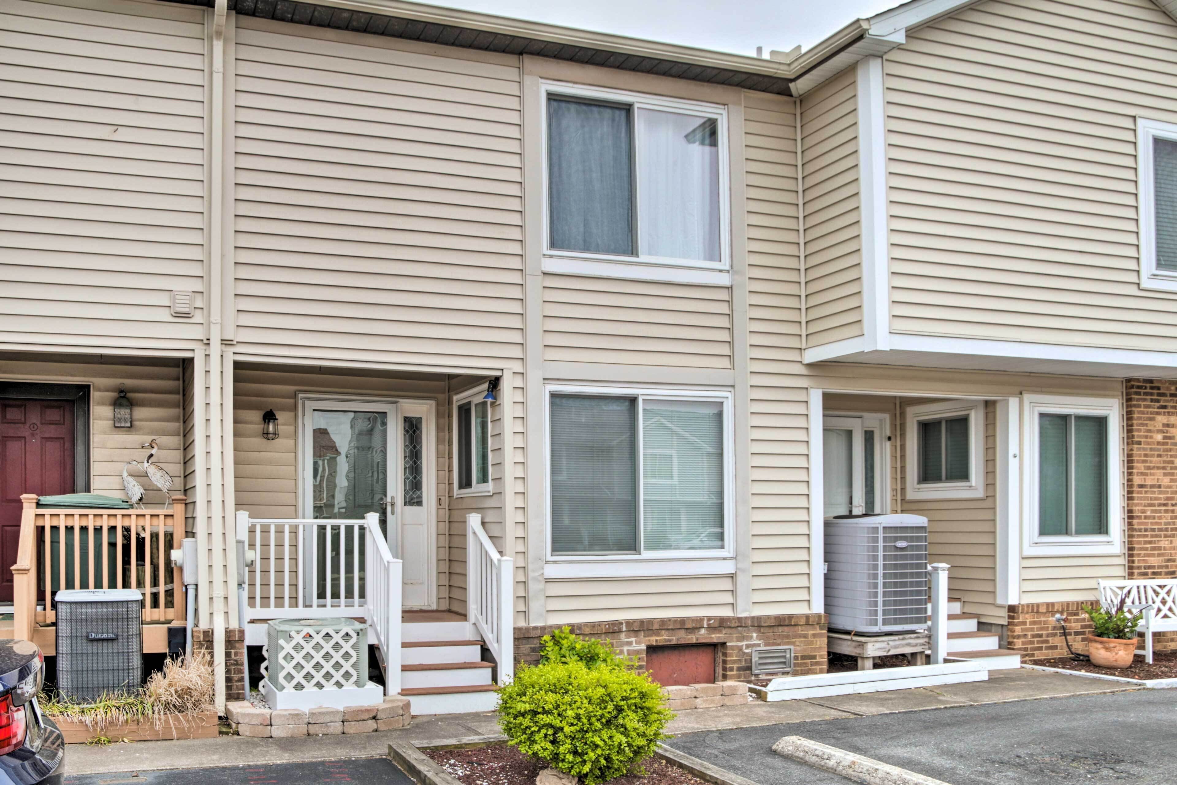 A two-story townhouse with a front porch, a small garden, and a parked vehicle.