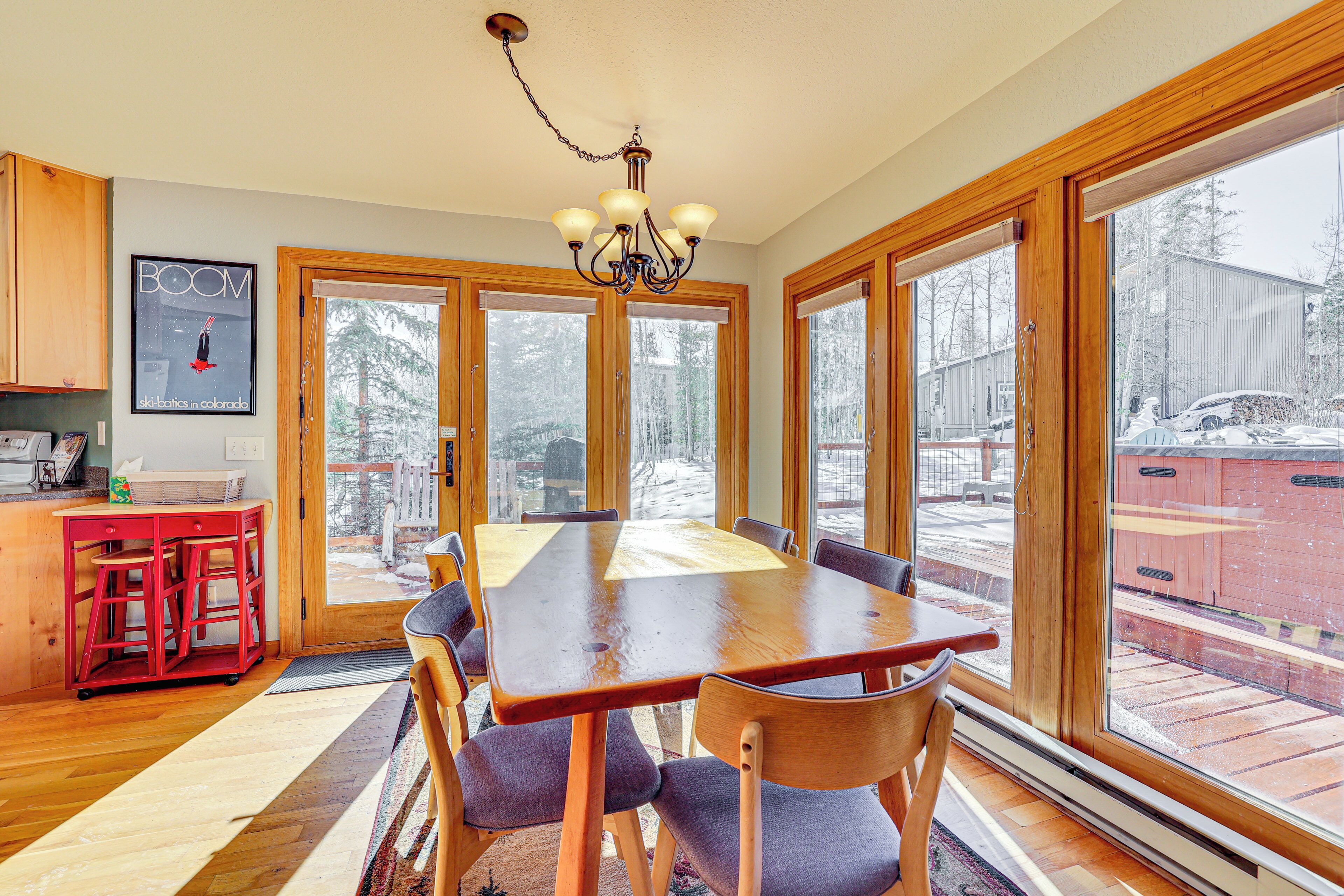 A dining area with a wooden table and chairs, large windows, and a chandelier.