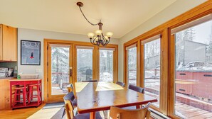 A dining area with a wooden table and chairs, large windows, and a chandelier. - 10 Mi to Keystone Resort: Cabin w/ Private Hot Tub (Silverthorne)