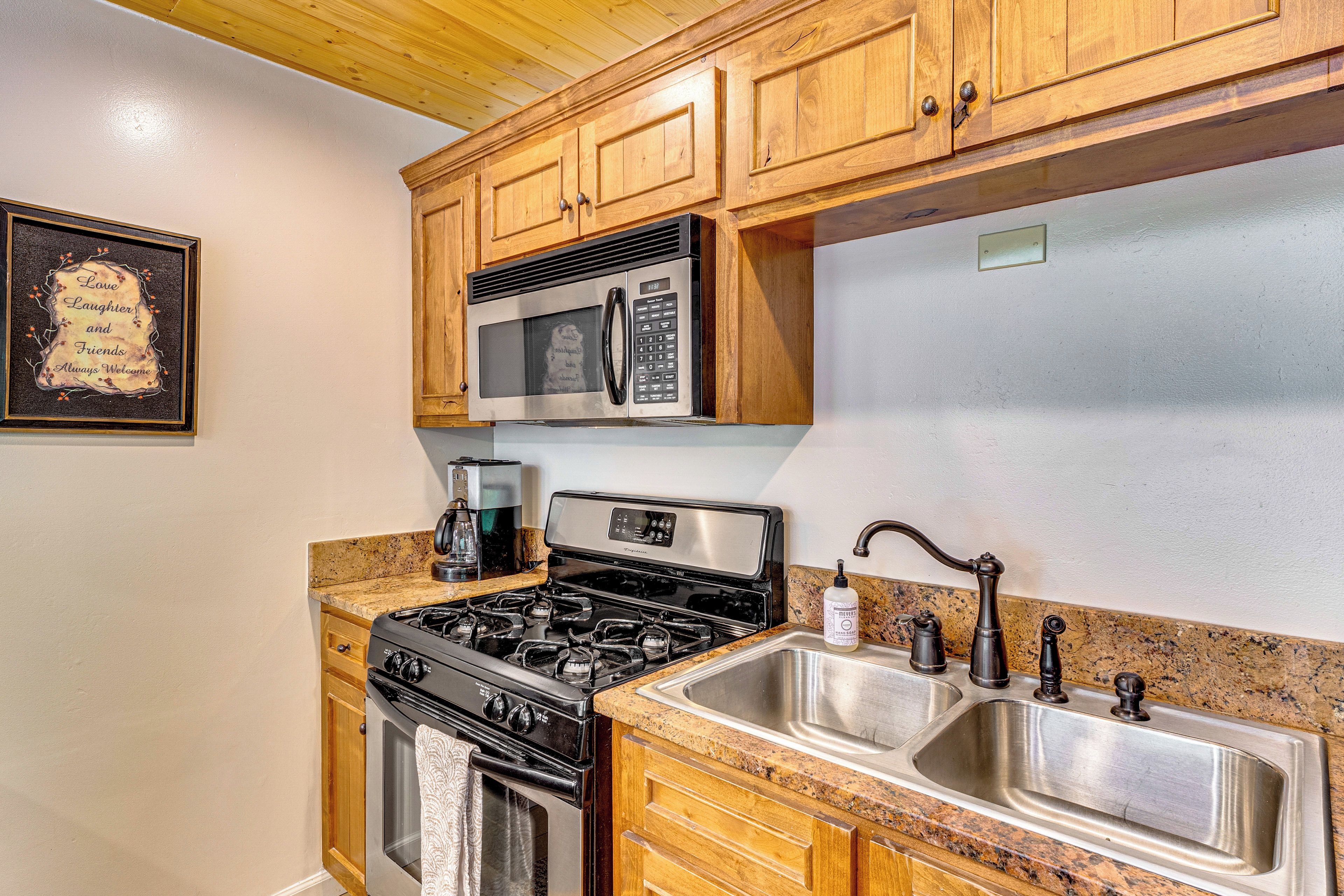 A kitchen with wooden cabinets, a stainless steel sink, a stove, and a microwave.