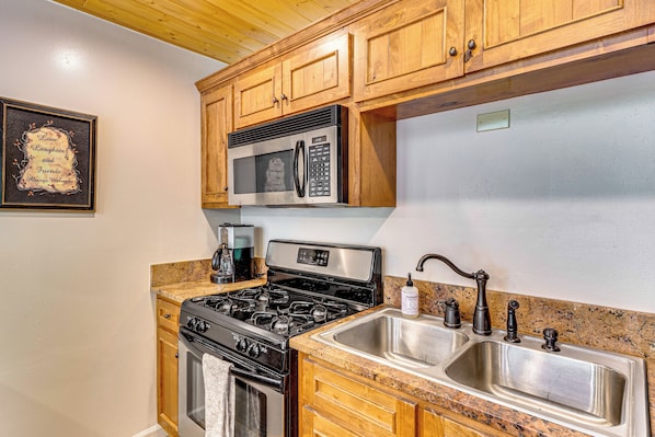 A kitchen with wooden cabinets, a stainless steel sink, a stove, and a microwave. - Cozy Streamside Studio - 2 Mi to Taos Ski Resort! (Taos Ski Valley)