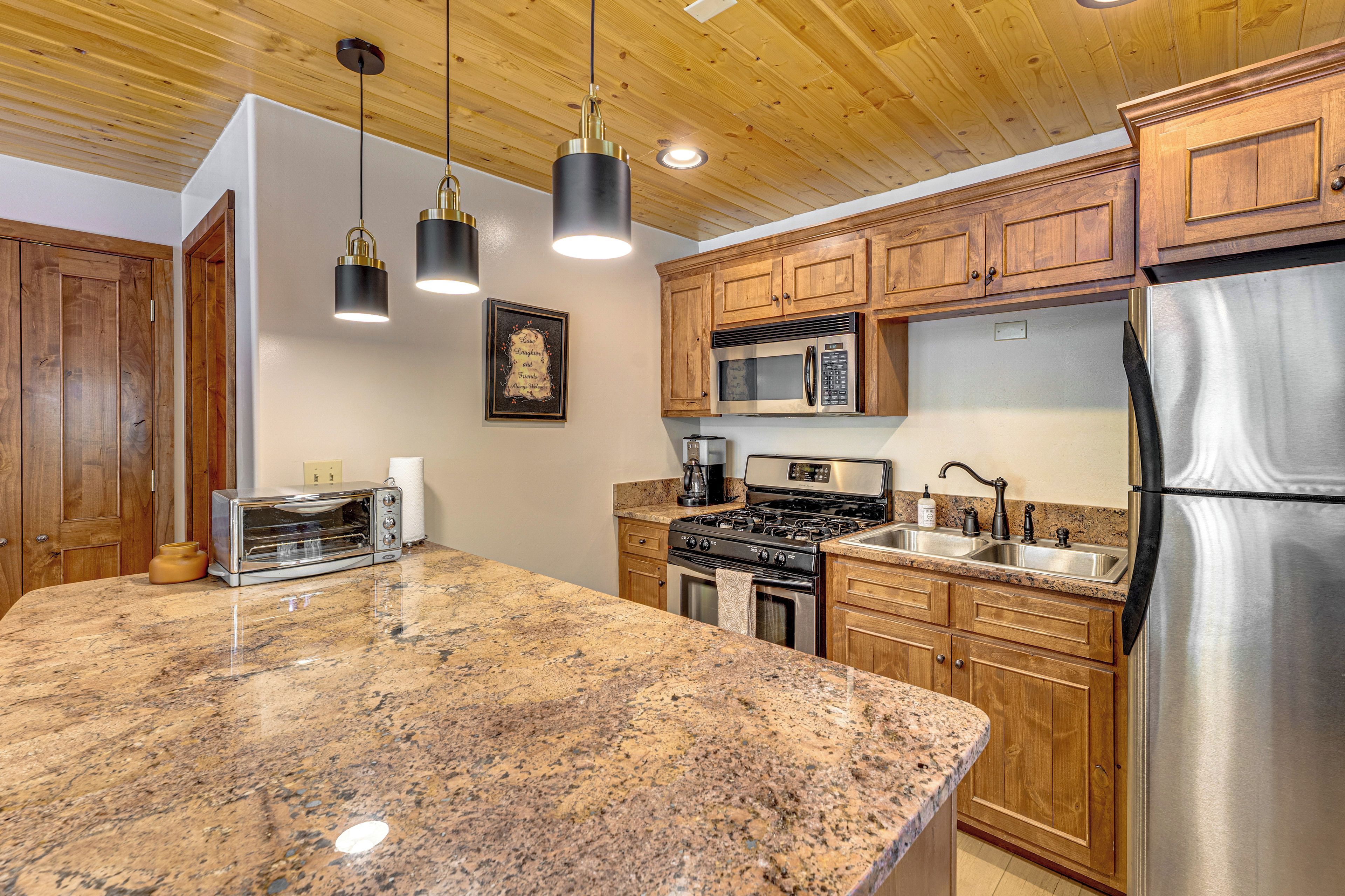 A kitchen with granite countertops, wooden cabinets, stainless steel appliances, and pendant lighting.
