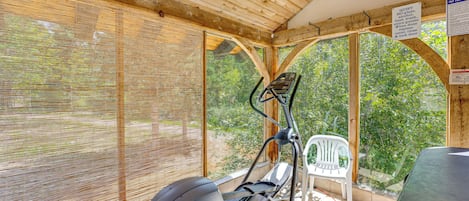 A covered outdoor gym area with exercise equipment, including a stationary bike and a rowing machine, and a white plastic chair.