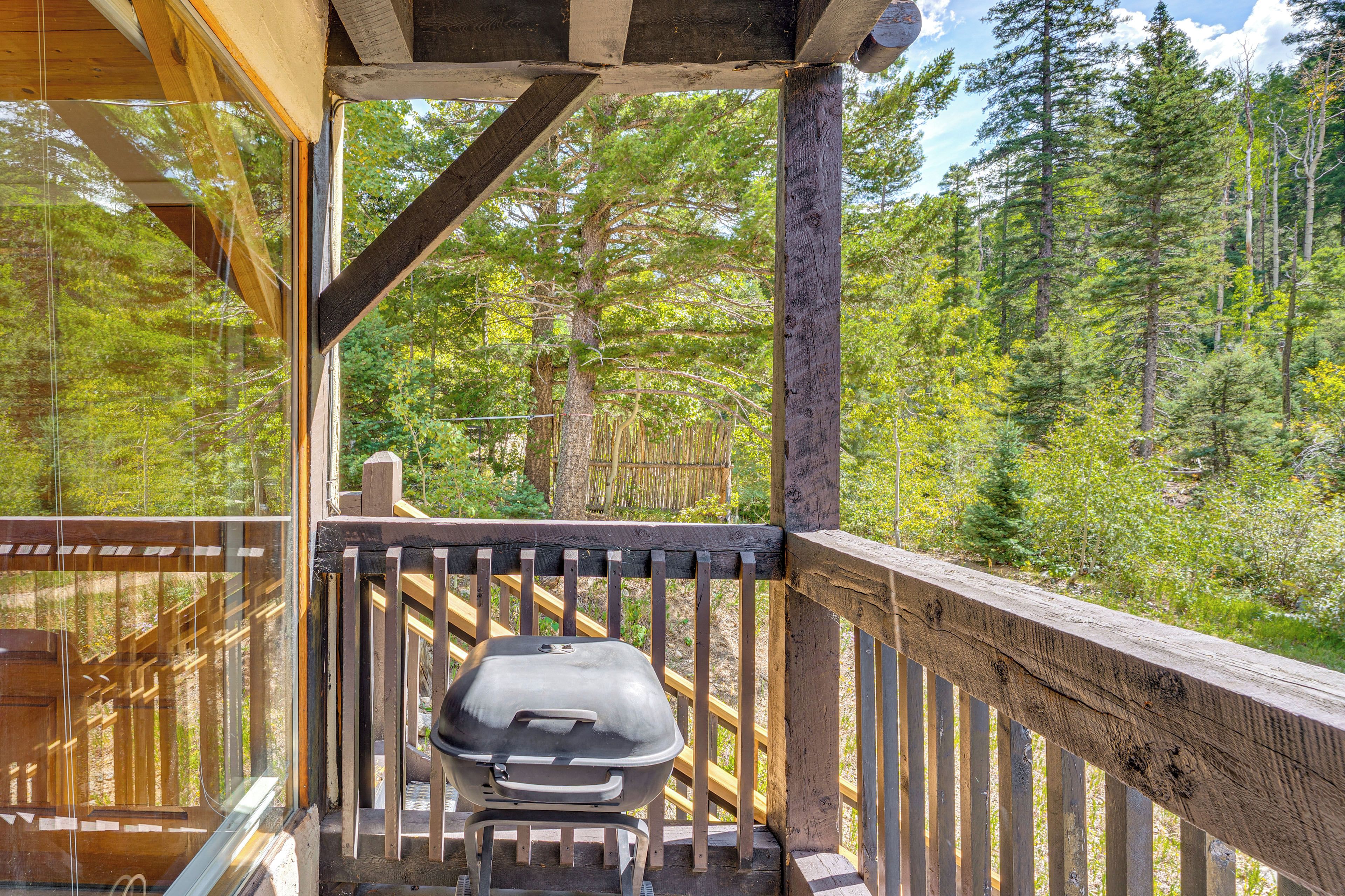 Une terrasse en bois avec un barbecue, donnant sur une zone boisée.