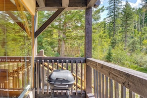 Eine Holzterrasse mit einem Grill, mit Blick auf ein bewaldetes Gebiet.