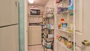 A compact kitchen with a microwave, washing machine, and organized shelves with various kitchen items.