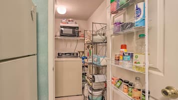 A compact kitchen with a microwave, washing machine, and organized shelves with various kitchen items.