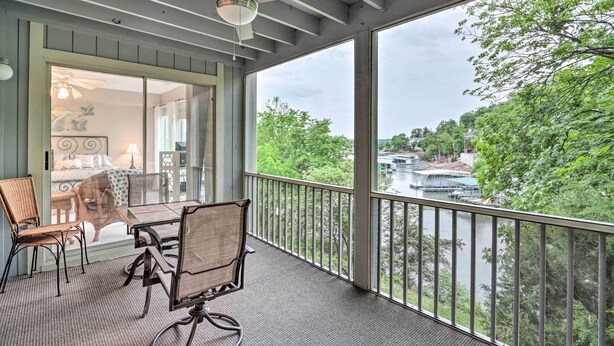 A balcony with a table and chairs, a ceiling fan, and a view of a river and greenery.