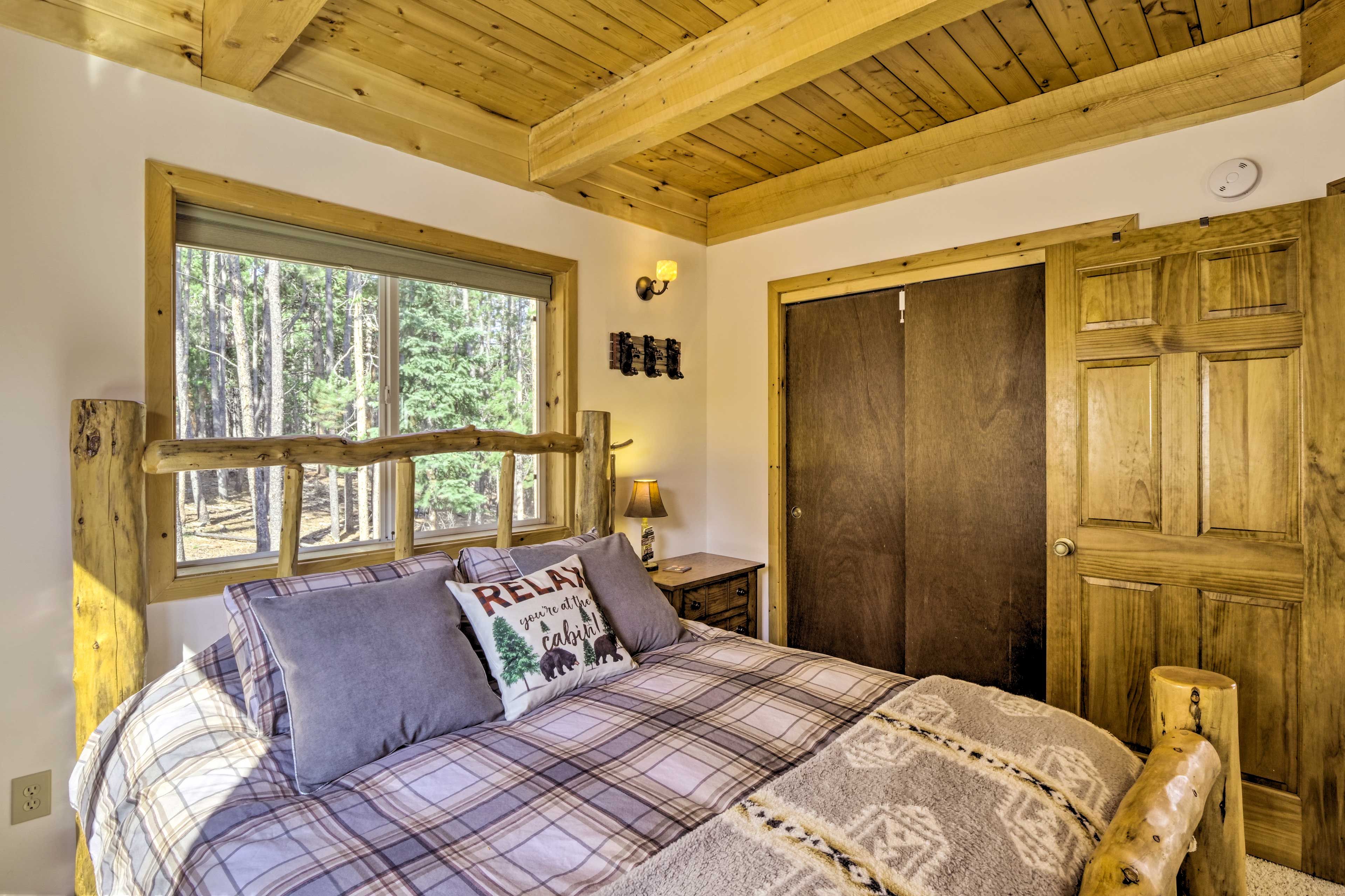 Una camera da letto con soffitto in legno, un'ampia finestra, un letto con copriletto a quadri e una porta in legno.
