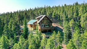 A wooden cabin with a deck, surrounded by a dense forest. - Secluded Fairplay Home w/ Hot Tub & Mountain Views (Fairplay)