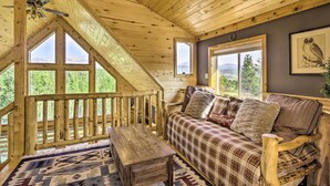A cozy cabin interior with a wooden ceiling, a plaid sofa, a wooden table, and large windows offering a view of the outdoors. - Secluded Fairplay Home w/ Hot Tub & Mountain Views (Fairplay)