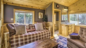 A cozy cabin interior with a plaid sofa, a wooden dining table, and a bathroom with a sink and mirror. - Secluded Fairplay Home w/ Hot Tub & Mountain Views (Fairplay)