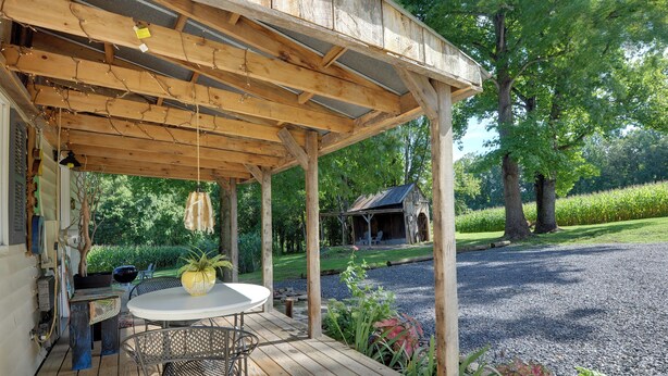 A wooden deck with a table and chairs, surrounded by greenery and a gravel path. - Secluded Lothian Farmhouse on 45 Acres w/ Fire Pit (Lothian)