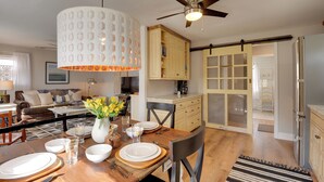 A dining area with a wooden table set for four, a ceiling fan, and a kitchen with wooden cabinets and a sliding door. - Secluded Lothian Farmhouse on 45 Acres w/ Fire Pit (Lothian)