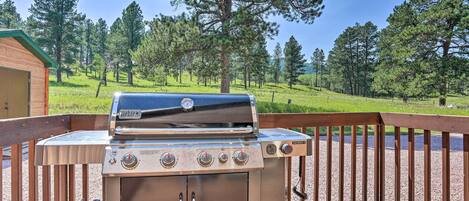A Weber gas grill on a wooden deck with a view of a forested area.