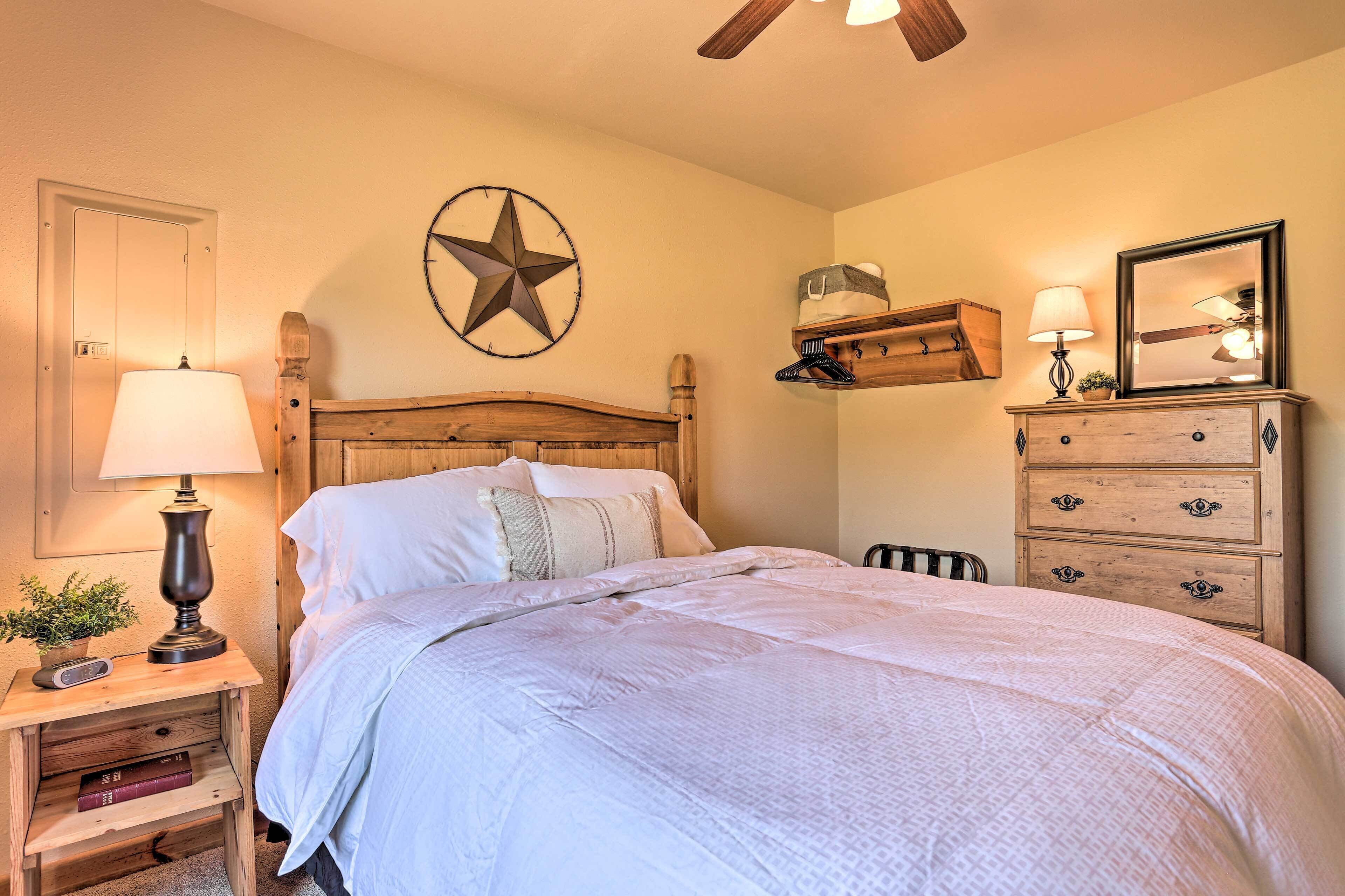 Une chambre avec un lit en bois, une table de chevet avec une lampe, une commode avec des tiroirs, une décoration murale en forme d’étoile et un ventilateur de plafond.