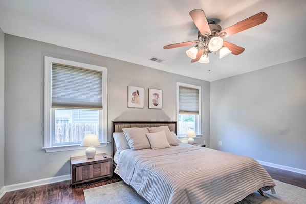 A bedroom with a bed, nightstands, a ceiling fan, and two windows with blinds.