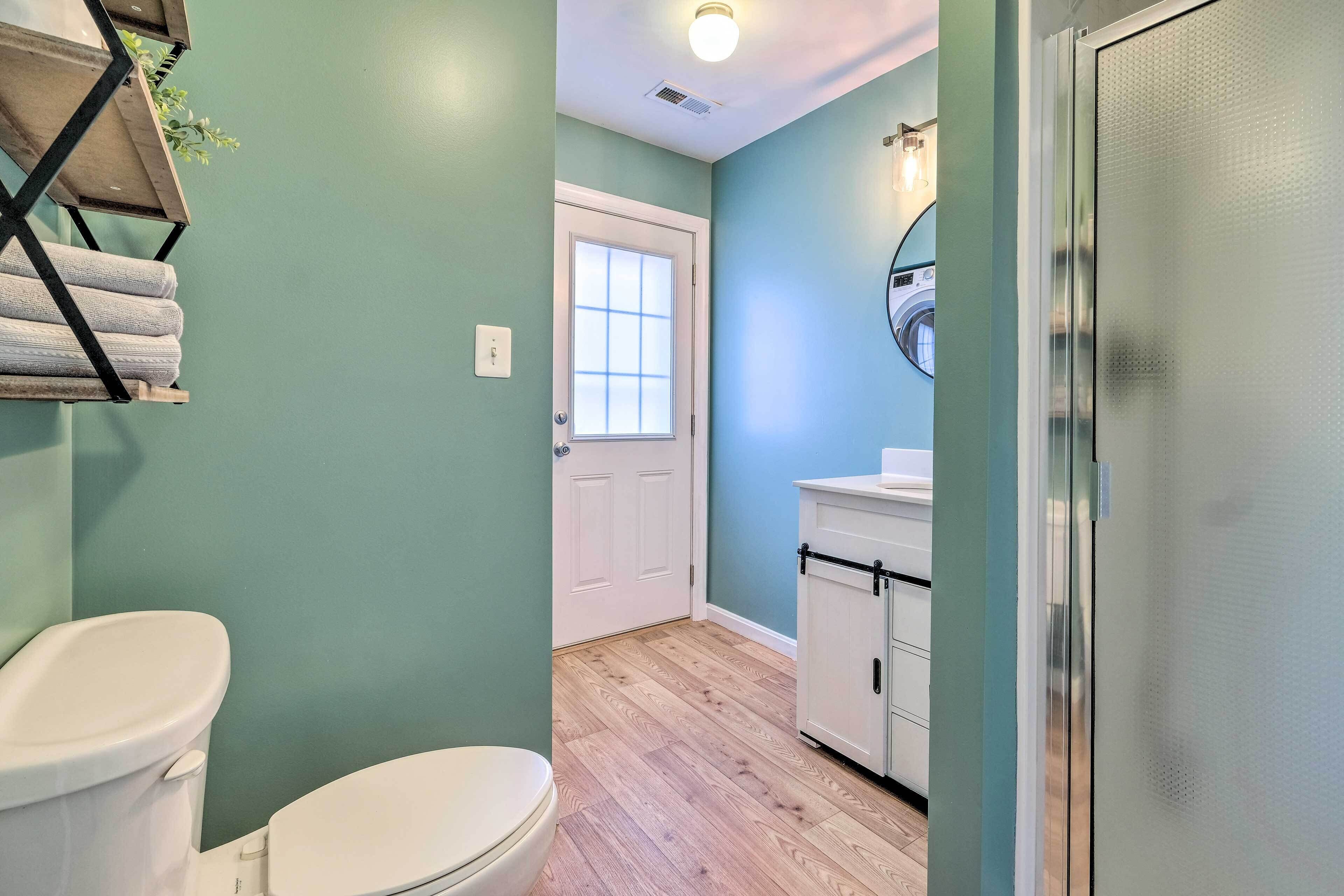 Un baño con inodoro blanco, lavabo con espejo y puerta que da a otra habitación.