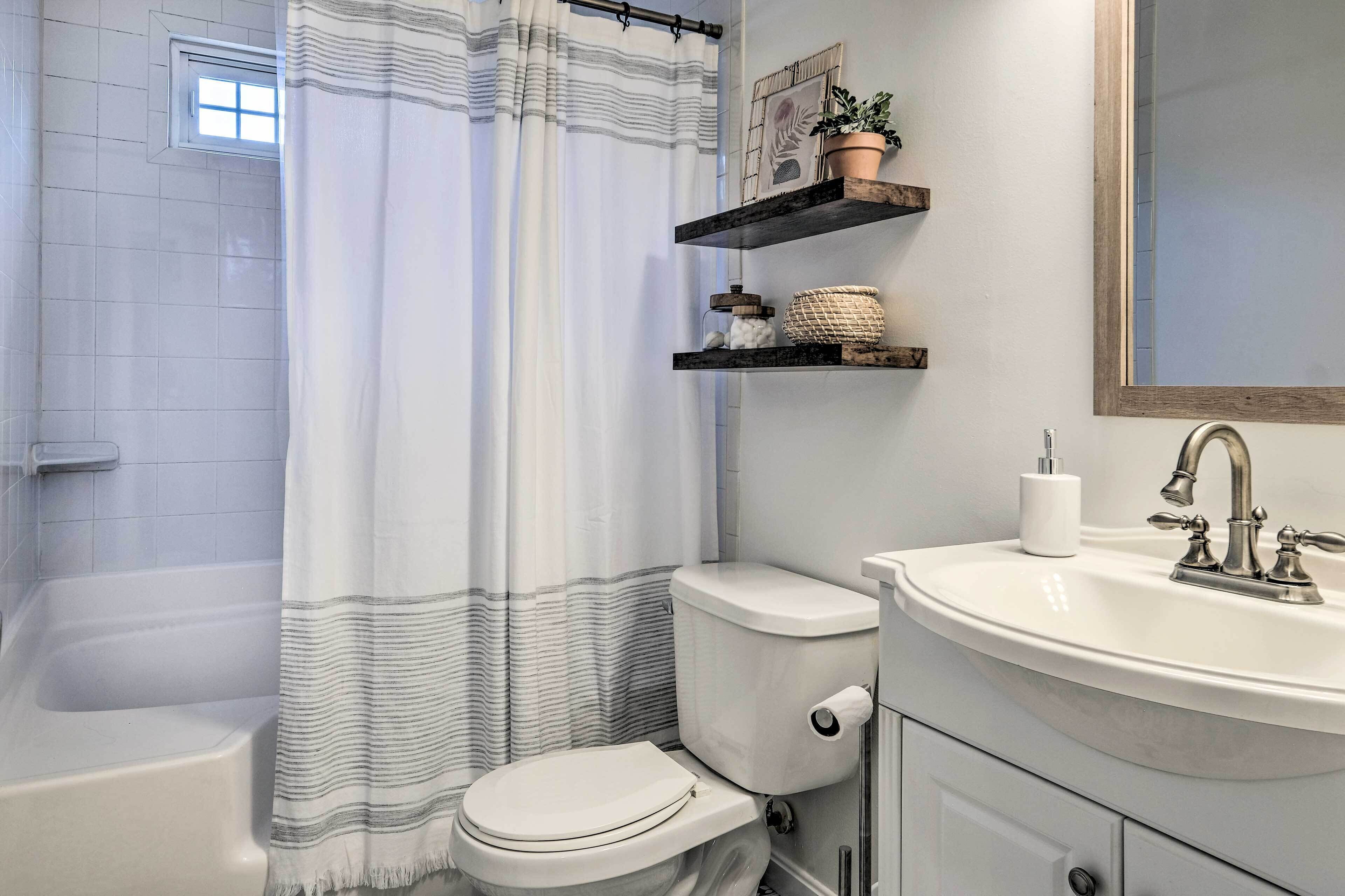 A bathroom with a bathtub, toilet, and sink. There are shelves above the sink with decorative items.