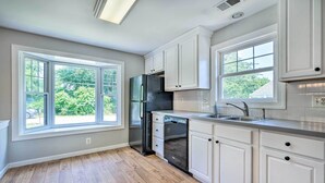 A kitchen with white cabinets, a stainless steel refrigerator, a dishwasher, and a window providing a view of greenery. - Idyllic Pasadena Retreat With Garden + Hot Tub! (Pasadena)