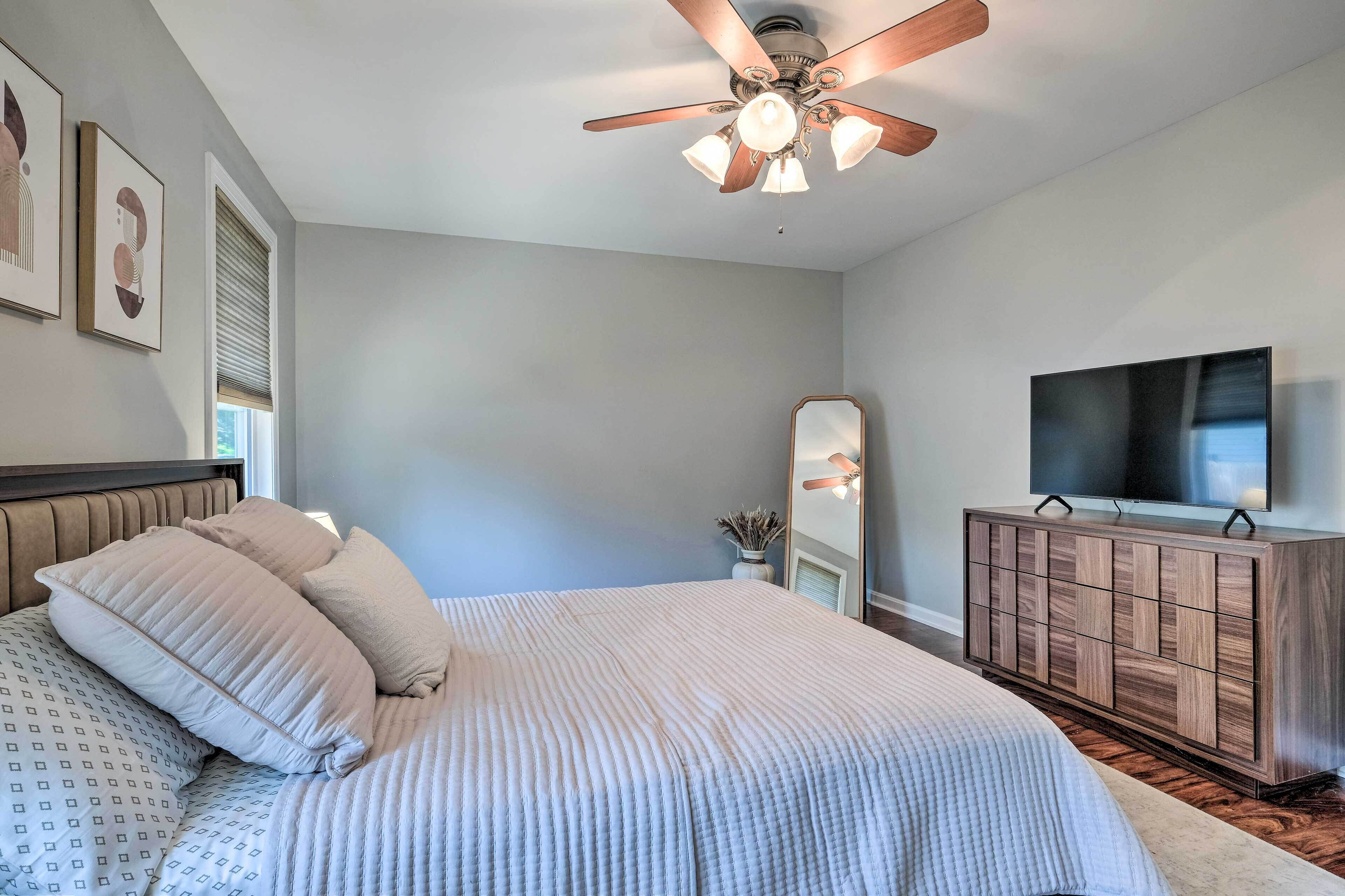 A bedroom with a bed, a ceiling fan, a TV, and a wooden dresser.