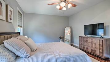 A bedroom with a bed, a ceiling fan, a TV, and a wooden dresser.