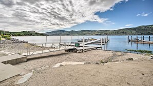 A lakeside dock with a concrete walkway leading to the water, surrounded by hills and a cloudy sky. - Lake Chelan Home in Private Community w/ Lake View (Manson)