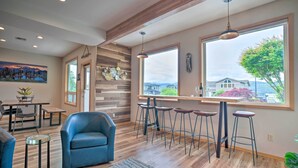 A modern kitchen with wooden accents, a dining area with a table and chairs, and a large window with a view of a house and trees. - Lake Chelan Home in Private Community w/ Lake View (Manson)