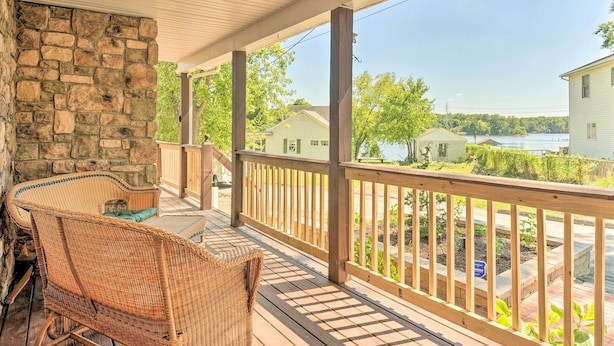 A covered porch with wicker furniture, stone walls, and a view of houses and water. - Sunny Glen Burnie Home - On-site Water Access (Glen Burnie)