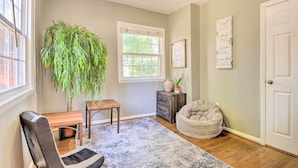 A room with a large window, a potted plant, a chair, a small table, a rug, a cabinet, and a door. - Sunny Glen Burnie Home - On-site Water Access (Glen Burnie)
