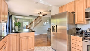 A modern kitchen with wooden cabinets, a stainless steel refrigerator, and a ceiling fan. - Sunny Glen Burnie Home - On-site Water Access (Glen Burnie)