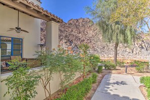 A residential area with a patio, a house with a beige exterior, a mountain backdrop, and a variety of plants.