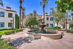 A courtyard with a central fountain, palm trees, and a building with a tiled roof and multiple windows.
