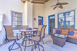 An outdoor patio with wicker furniture, a glass-top table, and a ceiling fan.
