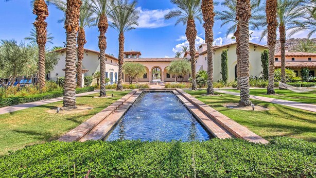 A pool surrounded by palm trees and a building with a tiled roof. - 243460: 3BR Desert Retreat w/ Views + Pool Access (La Quinta)