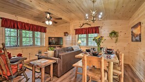 A cozy cabin interior with a wooden ceiling, a fireplace, a sofa, a dining table with chairs, and a television. - Secluded Mountain Cabin in Wardensville! (Wardensville)