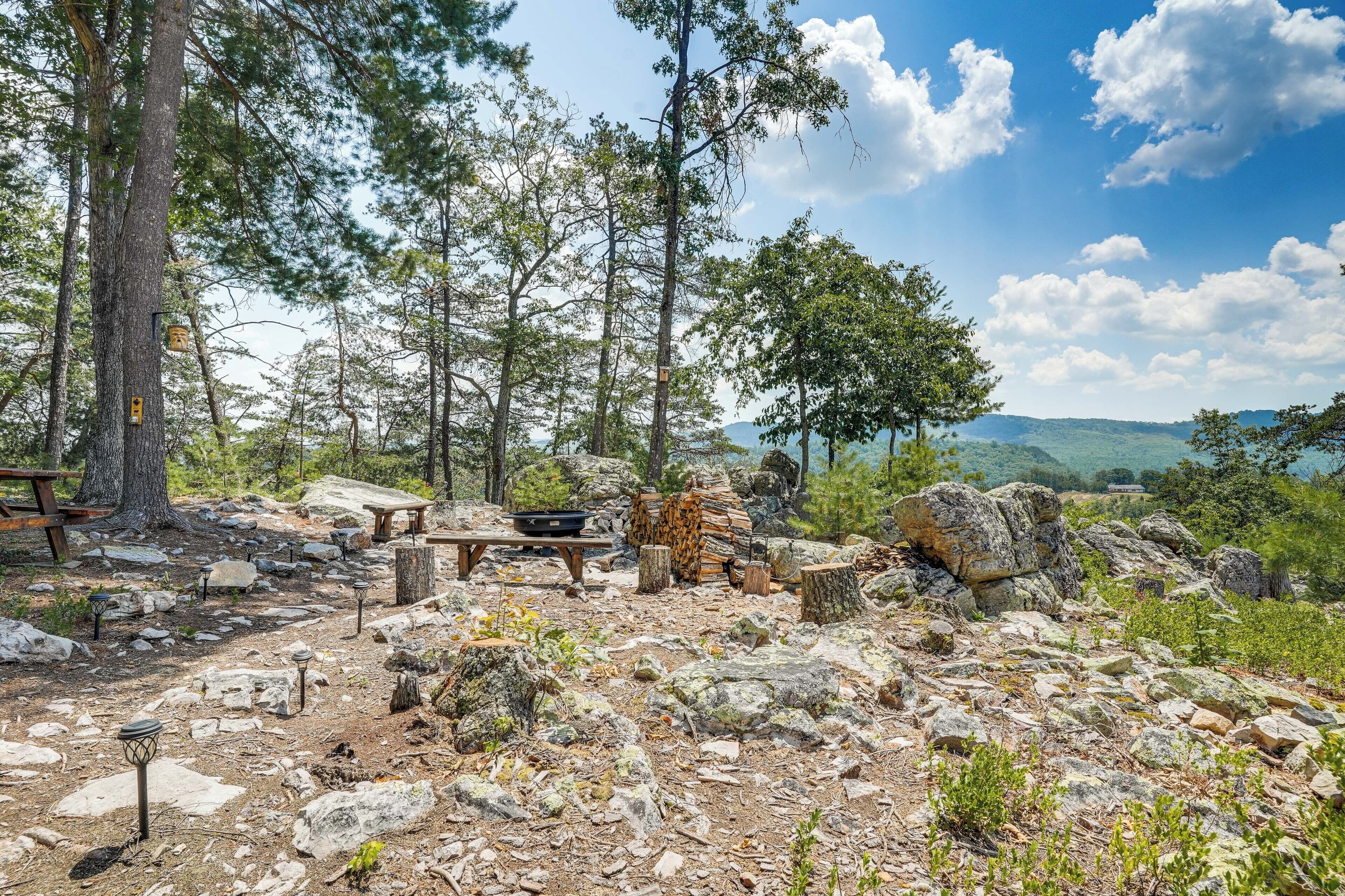 Eine rustikale Außenanlage mit Picknicktischen, einem Kamin aus Stein und Blick auf eine gebirgige Landschaft.