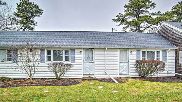 A single-story house with a grey roof, white siding, and a front door with a small porch. - Walk to Beach: Bright & Cozy Cape Cod Studio! (Dennis Port)