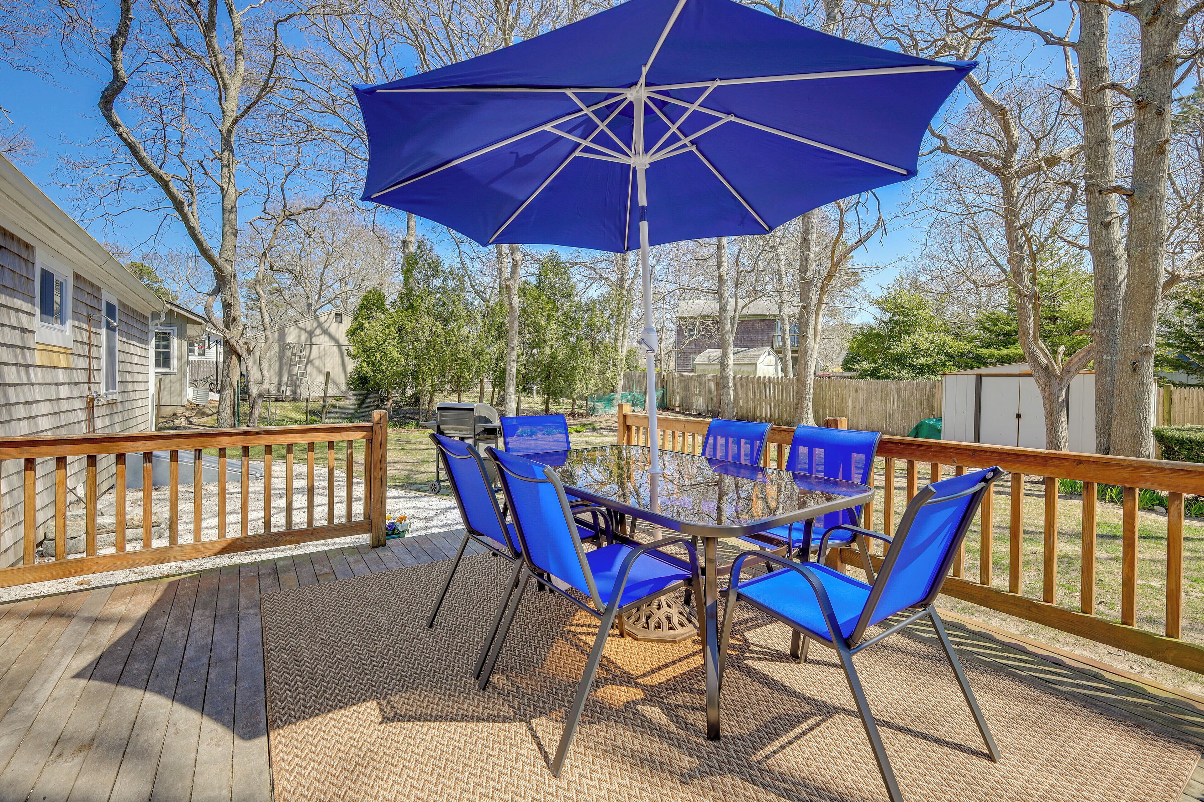 A deck with a table and chairs, a blue umbrella, and a wooden railing.